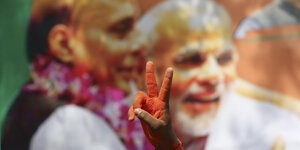 Eine Hand formt das "Peace-Zeichen", im Hintergrund ist Modis Gesicht zu sehen