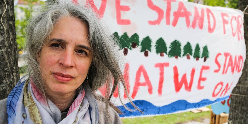 Eine Frau mit langen Haaren steht vor einen Plakat