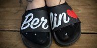 Füße, die in Adiletten stecken, auf denen das Wort "Berlin" steht - daneben ein Herz