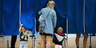 Eine junge Mutter betritt mit Kindern eine Wahlkabine.