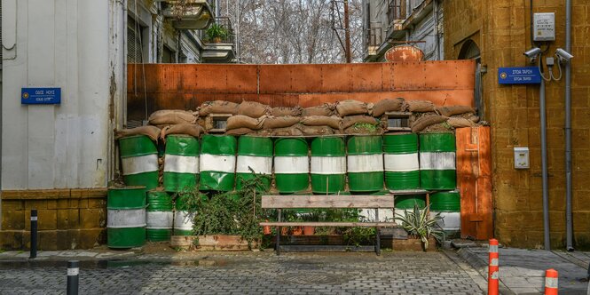 Fässer, Säcke und Trennwände, die eine Gasse versperren