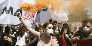Eine Demonstrantin hält eine orangene Rauchfackel in der Hand, während Schülerinnen und Schüler mit Protestplakaten und Bannern während des Fridays for Future