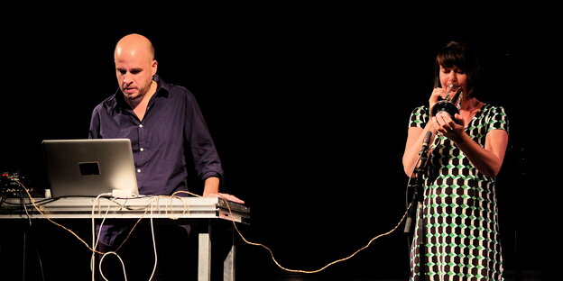 Eine Frau spielt auf einer Bühne Trompete, links neben ihr steht ein Mann an einem Laptop