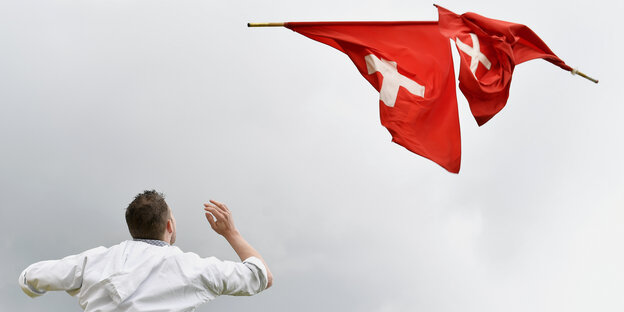 Ein Fahnenschwinger wirft zwei Schweizer Fahnen durch die Luft