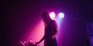 Lyra Pramuk an ihrem Synthesizer in einem Club, der mit violettem Licht erleuchtet ist