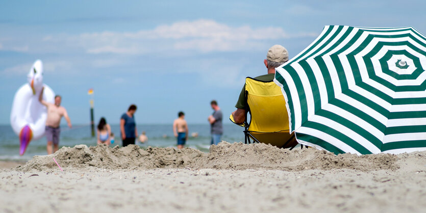 Urlauber sitzen bei hochsommerlichen Temperaturen unter einem Sonnenschirm