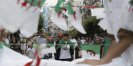 Mehrere DemonstrantInnen auf einer Straße, im Vordergrund, aber unscharf: algerische Fahnen