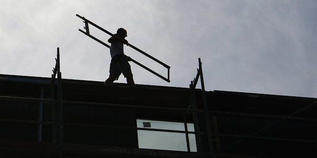 Ein Bauarbeiter trägt ein Gerüst über ein Dach.