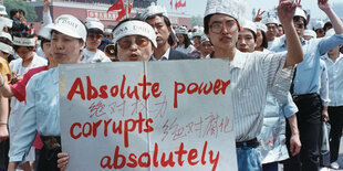 Protestierende auf dem Tienanmen-Platz. Sie tragen ein Transparent vor sich her, auf dem steht: Absolute power corrupts absolutely