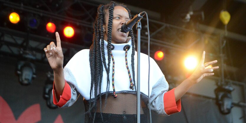 Jamila Woods steht vor einem Mikrofon und hebt beide Hände