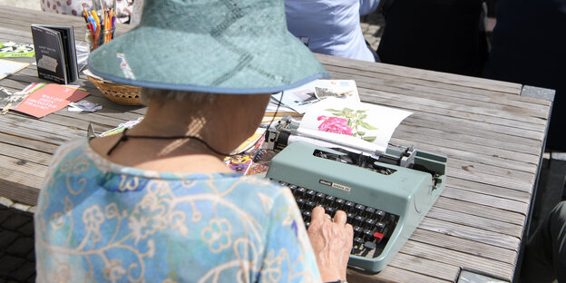Frau mit Hut schreibt auf historischer Schreibmaschine