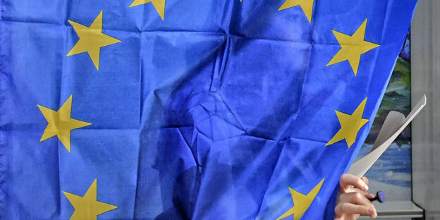 Eine Wählerin verlässt die Wahlkabine. Der Vorhang ist ene Europaflagge