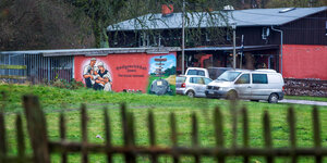 Hinter einem Holzzaun ist eine Garage mit der Aufschrift "Dorfgemeinschaft Jamel frei sozial und national" zu sehen, daneben stehen mehrere Autos