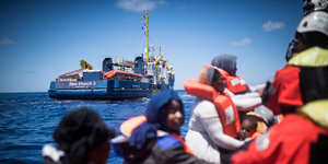 Im Mittelmeer gerettete Flüchtlinge treiben auf einem Boot, im Hintergrund ist das Schiff "Sea Watch 3" zu sehen