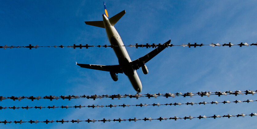 Flugzeug am Himmel, davor ist Stacheldraht zu sehen