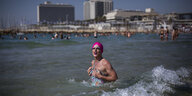 Eine Drag-Queen trägt eine pinkfarbene Bademütze und steht im Meer