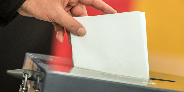 Jemand wirft einen Stimmzettel in einer Wahlurne vor einer Deutschlandflagge.