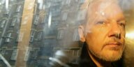 Assange guckt ernst - er sitzt hinter einer Autofensterscheibe
