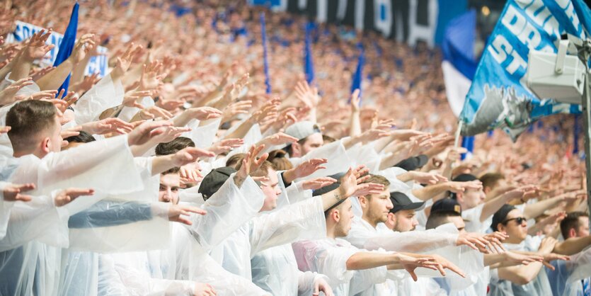 Fußballfans im Stadion tragen weiße Plastiksäcke, eine blaue Fahne von Schalke 04 wird geschwenkt