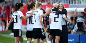 Mehrere deutsche Nationalspielerinnen stehen auf dem Fußballplatz, eine umarmt die Bundestrainerin Martina Voss-Tecklenburg