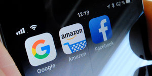 Auf einem Handydisplay sind die Logos von Google, Amazon und Facebook zu sehen