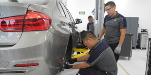 Zwei Männer stehen in einer Fabrik an einem Auto und arbeiten daran