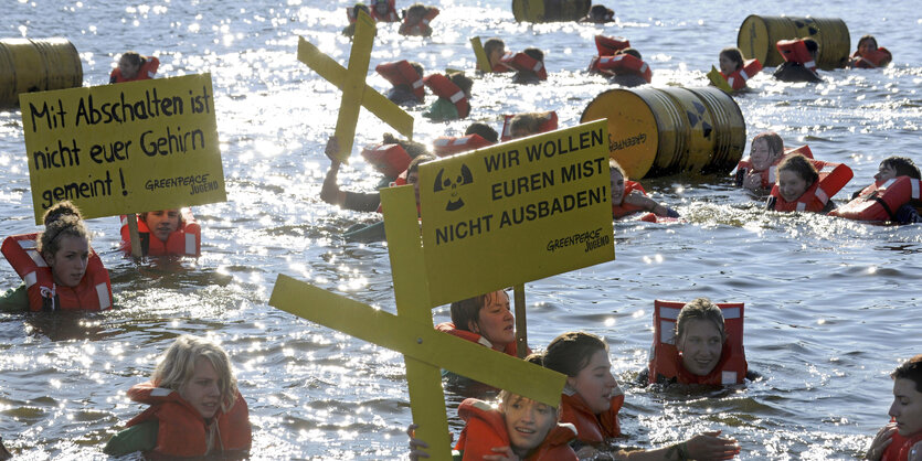 Jugendliche schwimmen im Wasser, tragen Rettungswesten und Schilder mit dem Schriftzug "Wir wollen Euren Mist nicht ausbaden"