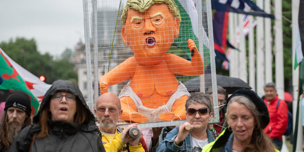 Demonstrierende tragen auf ihren Schultern eine Karrikaturfigur von US-Präsident Trump in einem Käfig