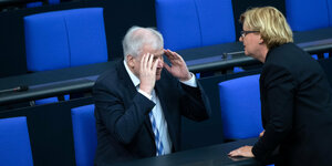 Bundesinnenminister Horst Seehofer (CSU) sitzt im Bundestag und spricht mit Eva Högl (SPD), die ihm gegenübersteht. Seine Hände verdecken sein Gesicht.