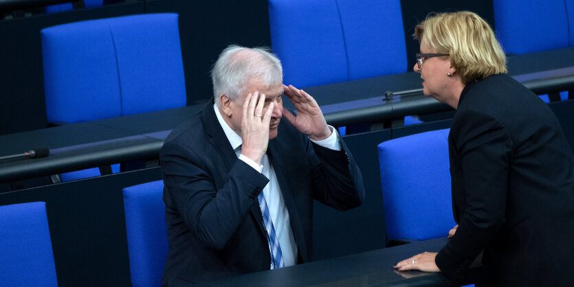 Bundesinnenminister Horst Seehofer (CSU) sitzt im Bundestag und spricht mit Eva Högl (SPD), die ihm gegenübersteht. Seine Hände verdecken sein Gesicht.