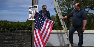Zwei Männer halten eine US-Fahne, an einem Mast bei ihnen steht eine Leiter