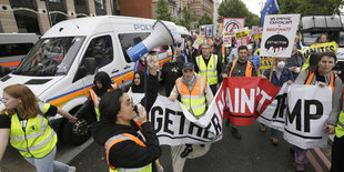 Menschen auf eienr Demonstration, einige halten einen Banner, eine Frau spricht durch ein Megafon