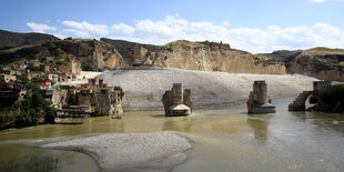 Die alte Stadt Hasankeyf am Tigris mit einer alten Brücke und historischen Bauten erstrahlt in der Abenddämmerung.