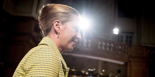 Oppositionsführerin Mitte Frederiksen, die die Wahlen gewann, steht in einem gelben Blazer im Scheinwerfergegenlicht.