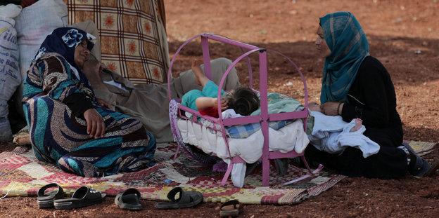 Zwei Frauen und ein kleines Kind unter freiem Himmel in einem Flüchtlingscamp