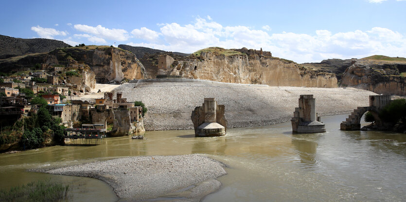 Die alte Stadt Hasankeyf am Tigris mit einer alten Brücke und historischen Bauten erstrahlt in der Abenddämmerung.