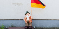 Ein Gartenzwerg steht vor einer Hauswand mit einer Deutschlandfahne in der Hand