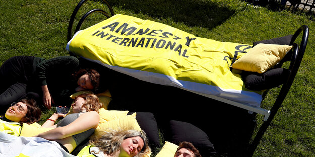 Menschen schlafen vor einem Bett mit "Amnesty International"-Bettdecke