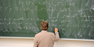 Ein Lehrer steht an einer Tafel und schreibt Formeln auf