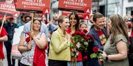Menschen halten „Mette Frederiksen“-Schilder hoch, zwischen ihnen steht eine lachende Frau , die einen Strauss rote Rosen hält