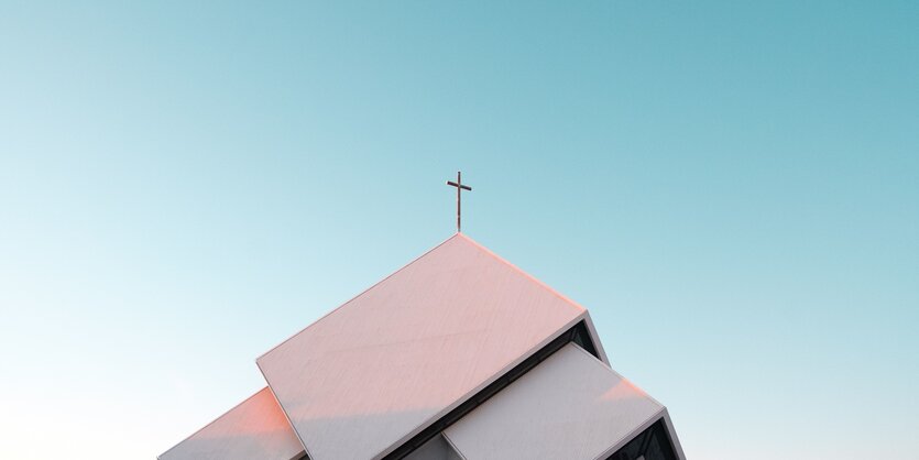 das Dach eines modernistischen Kirchenbaus - auf der Spitze ein goldenes Kreuz