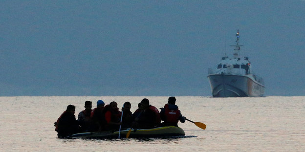 Menschen paddeln in einem Boot vor einem größeren Schiff