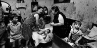 Fotografie in Schwarz/Weiß von Fauen und Kindern an einem Bett