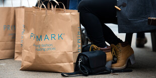 Taschen mit der Aufschrift „Primark“ stehen neben den Beinen einer Person