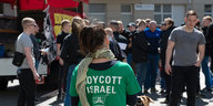 Eine Demonstrantin steht mit einem Shirt, auf dem "Boycott Israel" steht, auf dem Karl-Marx-Platz in Neukölln. Dort trafen sich nach Angaben der Polizei mehr als 100 Menschen zu einer linksradikalen und pro-palästinensischen Demonstration, zu der die Gru