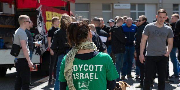 Eine Demonstrantin steht mit einem Shirt, auf dem "Boycott Israel" steht, auf dem Karl-Marx-Platz in Neukölln. Dort trafen sich nach Angaben der Polizei mehr als 100 Menschen zu einer linksradikalen und pro-palästinensischen Demonstration, zu der die Gru
