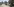 Ein afghanischer Polizist überquert eine Verkehrsinsel, neben ihm ist ein Autowrack zu sehen. Im Hintergrund sieht man mehr Polizei und Medienvertreter.