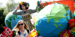 Aktivistinnen mit Blumenkränzen und einer Erde aus Pappmaschee