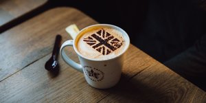 Eine Kaffeetasse mit Milchschaum. Darauf ist mit Kakaopulver die britische Flagge gestreut