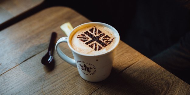 Eine Kaffeetasse mit Milchschaum. Darauf ist mit Kakaopulver die britische Flagge gestreut